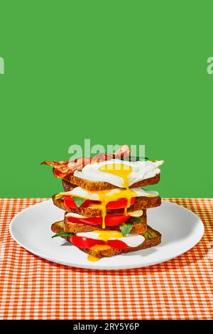 Toast bread, fiend eggs, bacon, tomatoes and basil on plate on checkered tablecloth over green background. Breakfast. Pop art Stock Photo