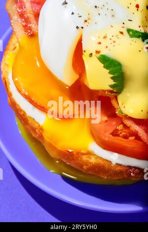 Close-up of poached eggs with liquid yolk, tomato, bacon and cheese sauce on toasted bun. Breakfast, food. Pop art Stock Photo