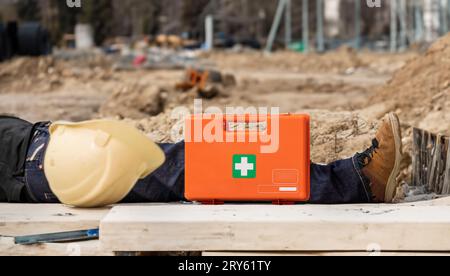 Symbol for an work accident. Man lies on the ground next to a first aid kit and a helmet. Stock Photo