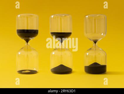 Like sands through the hourglass, so are the days of our lives. Creative hourglass, sandglass, sand timer or sand clock against yellow background. Stock Photo