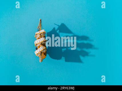 Old ship traveling on the sea. Sailing boat and shadow on blue background composition. Travel, vacation and summer journey concept. Summer flat lay. Stock Photo