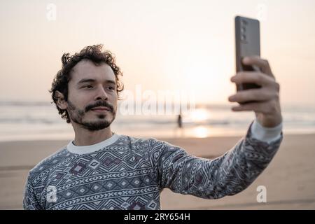 Young man takes a selfie photo on the beach at sunset Stock Photo