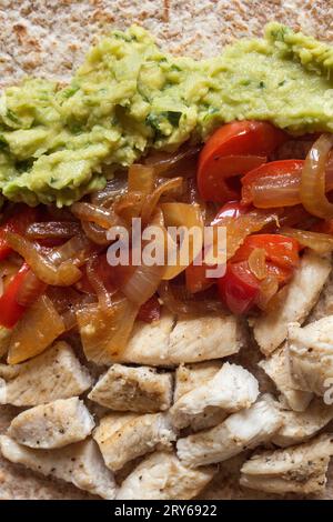 A close-up overhead view of homemade Mexican fajita ingredients featuring guacamole, cumin-seasoned chicken, onion, and semi-raw red pepper, artfully Stock Photo