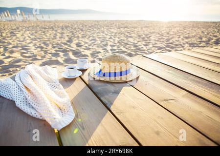 a hat, a cape and two cups of coffee stand on a pier near the sea. Stock Photo