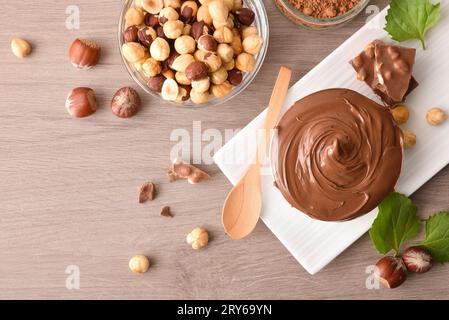 Chocolate cream and hazelnut in bowls with portions of chocolate nuts and leaves on wooden table. Top view. Stock Photo