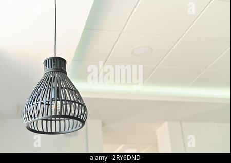 A beautiful lamp on a long wire hangs on the ceiling. against a white wall. Stock Photo