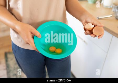 a woman breaks chicken eggs in a bowl while standing in the kitchen Stock Photo