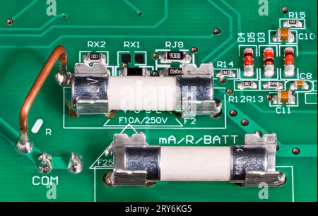 Close-up of ceramic tubes of electrical fuses in metal holder on circuit board. Low ohm wire resistor for current measuring, capacitors or red diodes. Stock Photo