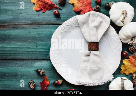 Flat lay of a white plate with napkin. Place setting over a rustic wood table with colorful autumn leaves. Table top view. Stock Photo