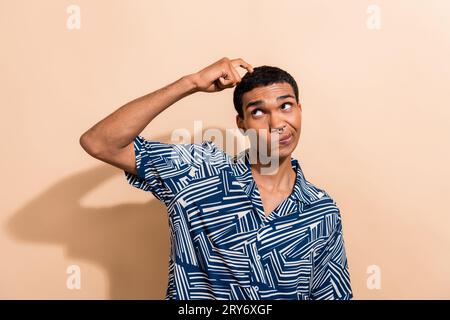 Photo portrait of handsome young guy scratch head confused skeptical wear trendy blue print outfit isolated on beige color background Stock Photo
