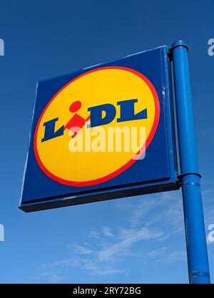 Sign and logo of a Lidl supermarket. Blue sky in the background. Lidl is a German retail group known for its low prices Stock Photo