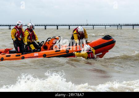 RNLI crew pulling a fellow crewman aboard an inshore lifeboat from a rough Thames Estuary off Southend on Sea, Essex, UK. Training exercise Stock Photo