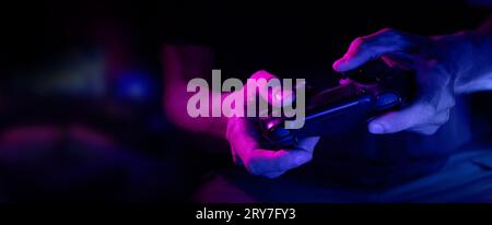 closeup of wireless video game controller in gamer hands in neon lights. banner with copy space Stock Photo