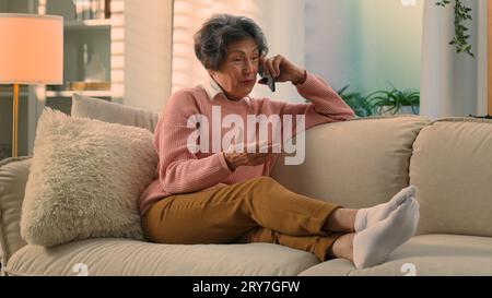 Happy old woman relaxing on cozy sofa talking on smartphone smiling senior grandma at comfy couch at home distant talk cellphone call elderly lady Stock Photo