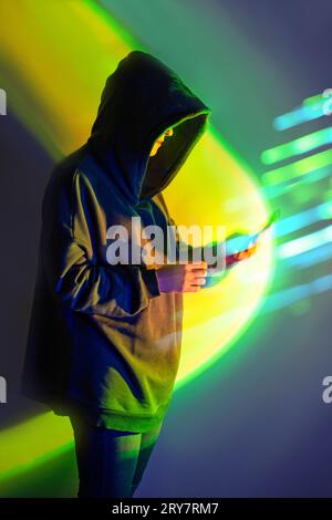 Safe storage of personal data on a smartphone. Shrouded in darkness hooded figure  with phone on vivid neon background. Stock Photo
