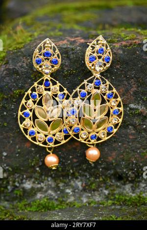 closeup the pair of golden blue color ear ring on the green brown stone soft focus natural green brown background. Stock Photo