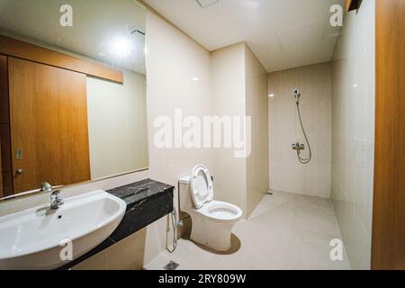 The bathroom of a new apartment with a wash basin attached to the wall is equipped with glass and a sitting closet. Stock Photo