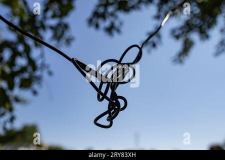 electrical cable knot on blue sky background with defocused tree leaves Stock Photo