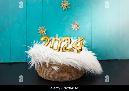 New born photography backdrop with white fur, straw snowflakes, 2024 golden balloons number and blue painted wood boards. Stock Photo