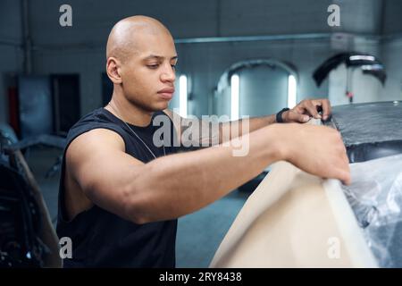 Focused automobile mechanic covering car parts with special protective paper Stock Photo