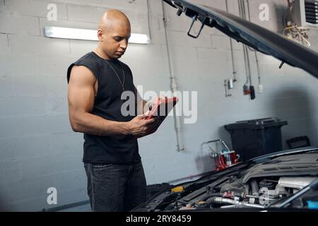 African American auto-mechanic using tablet to check electronic system of car Stock Photo