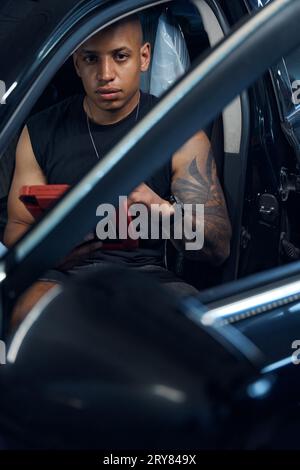 Serious auto-mechanic installing on car on-board computer using tablet Stock Photo