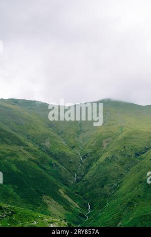 Running waterfall on a cloudy valley in Vall de Nuria Stock Photo