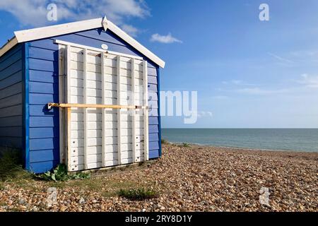 Blue beach hut with a white door stands agains blue sky and sea at the beach. Southampton, United Kingdom, England Stock Photo