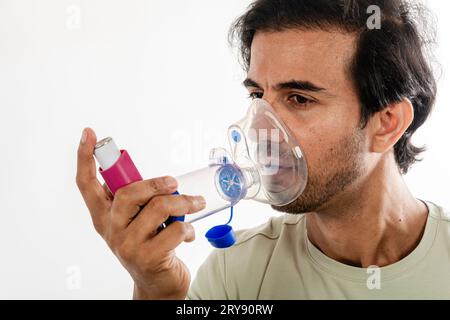 Asian young man from india using a respiratory inhaler. Study shot on white background, selective focus. Stock Photo