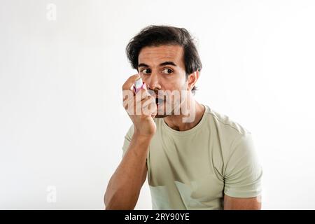 Asian young man from india using a respiratory inhaler. Study shot on white background, selective focus. Stock Photo