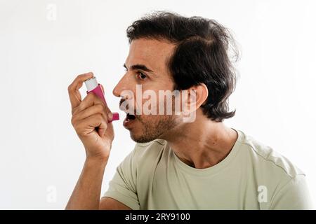 Asian young man from india using a respiratory inhaler. Study shot on white background, selective focus. Stock Photo