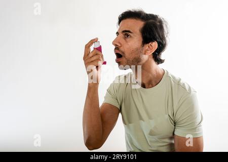 Asian young man from india using a respiratory inhaler. Study shot on white background, selective focus. Stock Photo