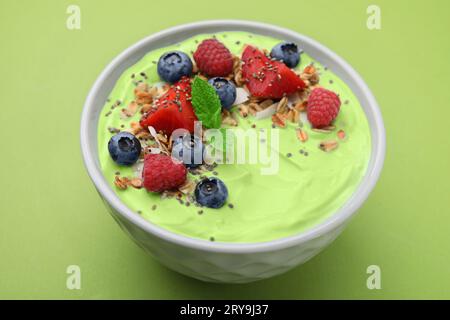 Tasty matcha smoothie bowl served with berries and oatmeal on green background. Healthy breakfast Stock Photo