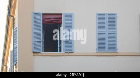 Closed window with shutters and one open on a white wall of the building in the city. Stock Photo