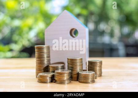 Coins stack in front of wooden home on wooden table, Save money concept, Property investment, house loan, reverse mortgage, gold coins money stack gro Stock Photo
