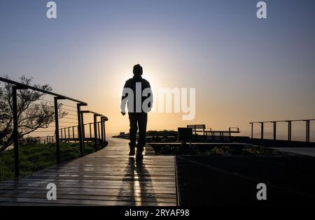 Silhouette image of man walking on boardwalk around the crater at sunrise. Mt Eden Summit. Auckland. Stock Photo