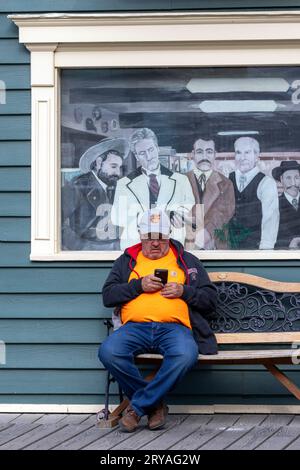 Man sitting on a bench with his cell phone in Skagway, Alaska, USA Stock Photo
