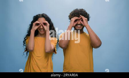 Studio portrait Indian family Arabian couple Hispanic man woman looking through hands make circles shape binoculars eyewear glasses goggles eyeglasses Stock Photo
