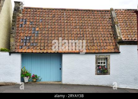 Quaint cottage with whitewashed stucco walls, potted flowers on the windowsill and in front of a pale blue door panel and vintage clay tile roof Stock Photo