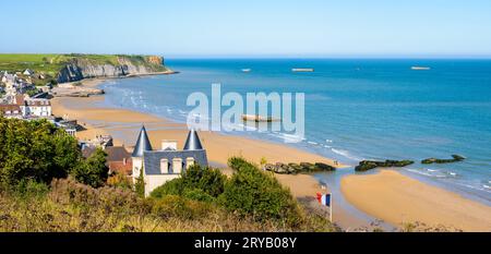 View over Arromanches beach in Normandy on a sunny day with remains of the WWII Mulberry harbour lying on the sand and the Phoenix caissons in the sea Stock Photo