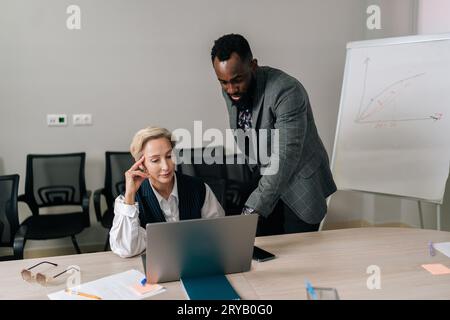Portrait of helpful middle-aged female mentor teaching African-American intern student, talk instruct, help young trainee with computer work. Stock Photo