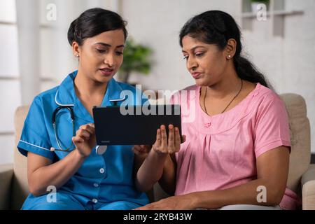 Indian nurse explaining from digital tablet to woman patient about health condition at home - concept of medical guidance, health care support and Stock Photo