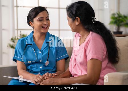 Side view shot of happy indian nurse with talking with recovered woman patient on sofa during home visit - concept of health care support Stock Photo