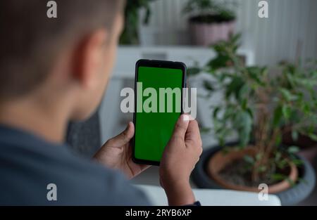 Boy is holding a smartphone in front of him . Green screen, copy space and chroma key on smartphone screen. Stock Photo
