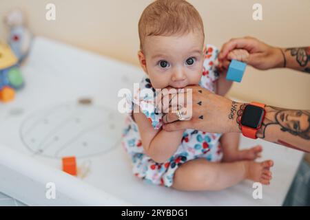 Young mom playing with her baby girl in a hospital before check up. Cute baby girl biting moms finger. Gorgeous baby girl looking at camera. Child hea Stock Photo