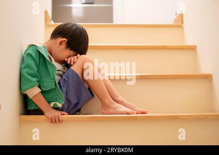 A sad Asian boy sits with his head down on the steps.   sad Stock Photo