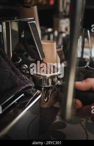 Barista preparing coffee in coffee machine with equipment - vertical photo. Closeup of coffee making process. Hands of barista using a coffee machine. Stock Photo