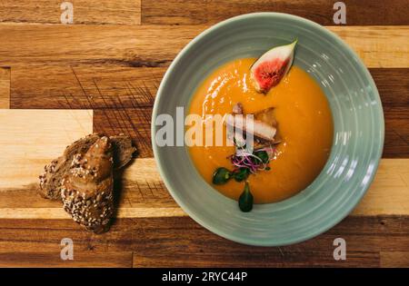 The cod fish fillet with orange soup from sweet potatoes and other tasty ingredients. Top view of food with fresh baguette on wooden background - phot Stock Photo