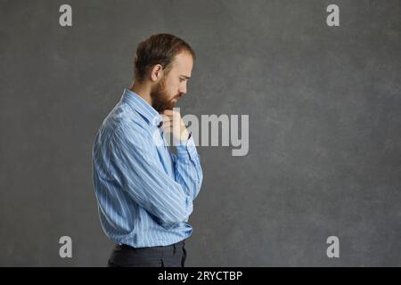 Pensive business man touching beard looking down standing over grey wall Stock Photo