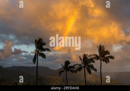 Sunrise illuminates storm clouds and rainbow over Hanalei mountains from Princeville overlook of bay Stock Photo